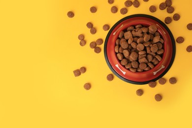 Photo of Dry dog food and feeding bowl on orange background, flat lay. Space for text