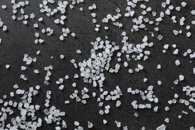 Scattered white natural salt on black table, top view