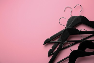 Black hangers on pink background, top view. Space for text