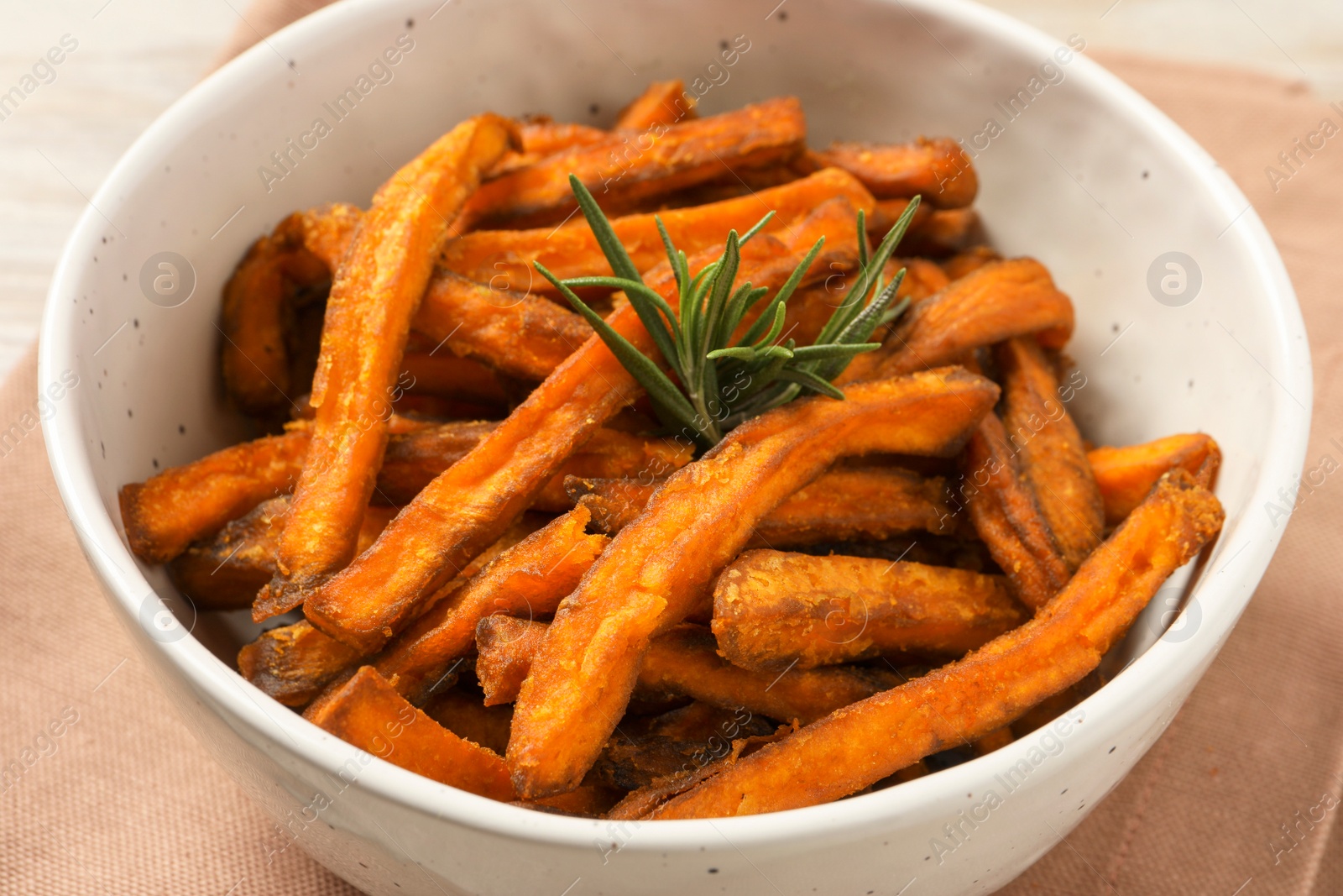 Photo of Bowl with sweet potato fries and rosemary on beige cloth, closeup