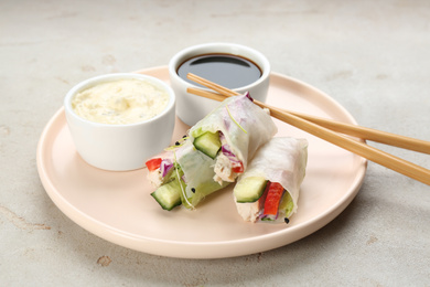 Photo of Delicious rolls wrapped in rice paper served on light grey table