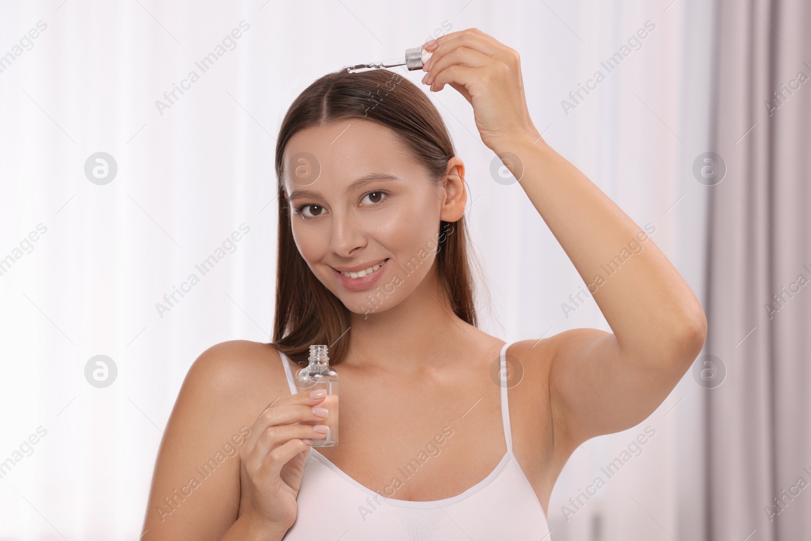 Photo of Beautiful woman applying serum onto hair indoors