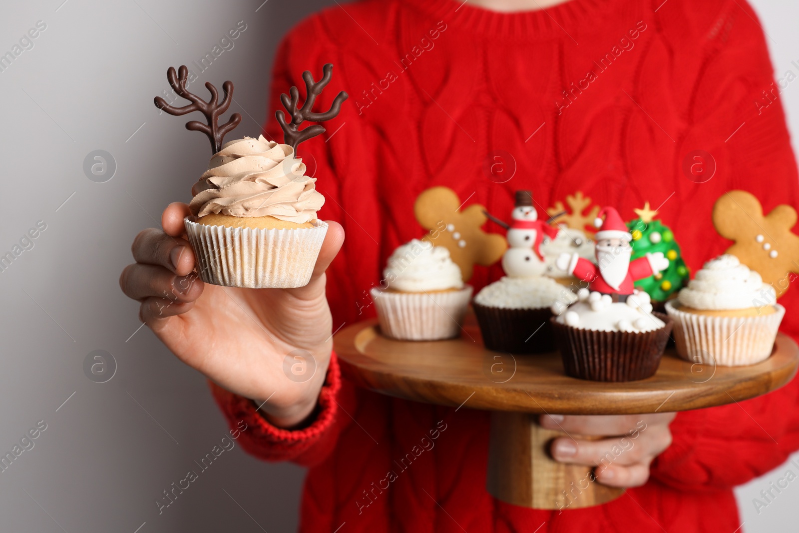 Photo of Woman holding tasty Christmas cupcakes on light background, closeup