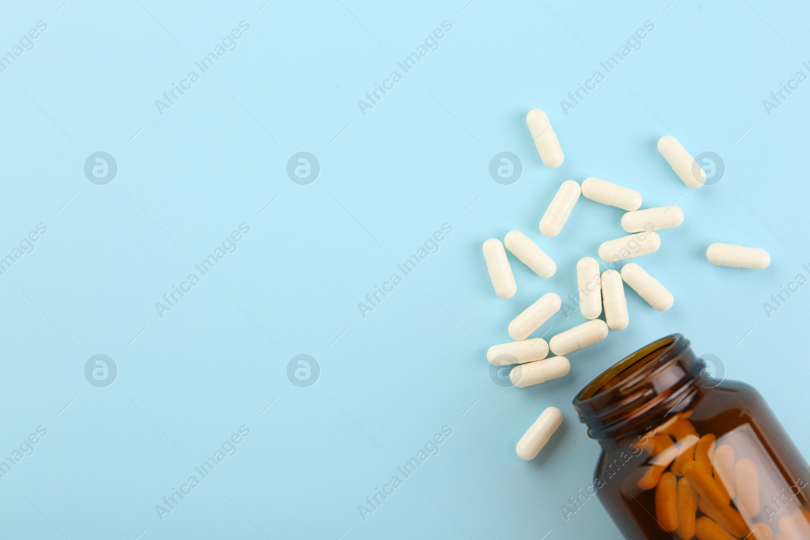 Photo of Bottle and vitamin capsules on light blue background, top view. Space for text