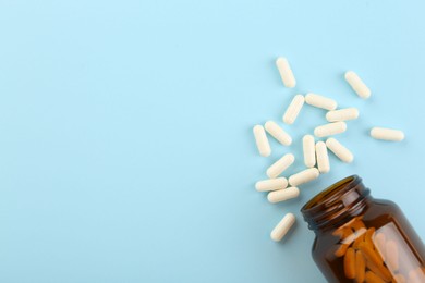 Photo of Bottle and vitamin capsules on light blue background, top view. Space for text