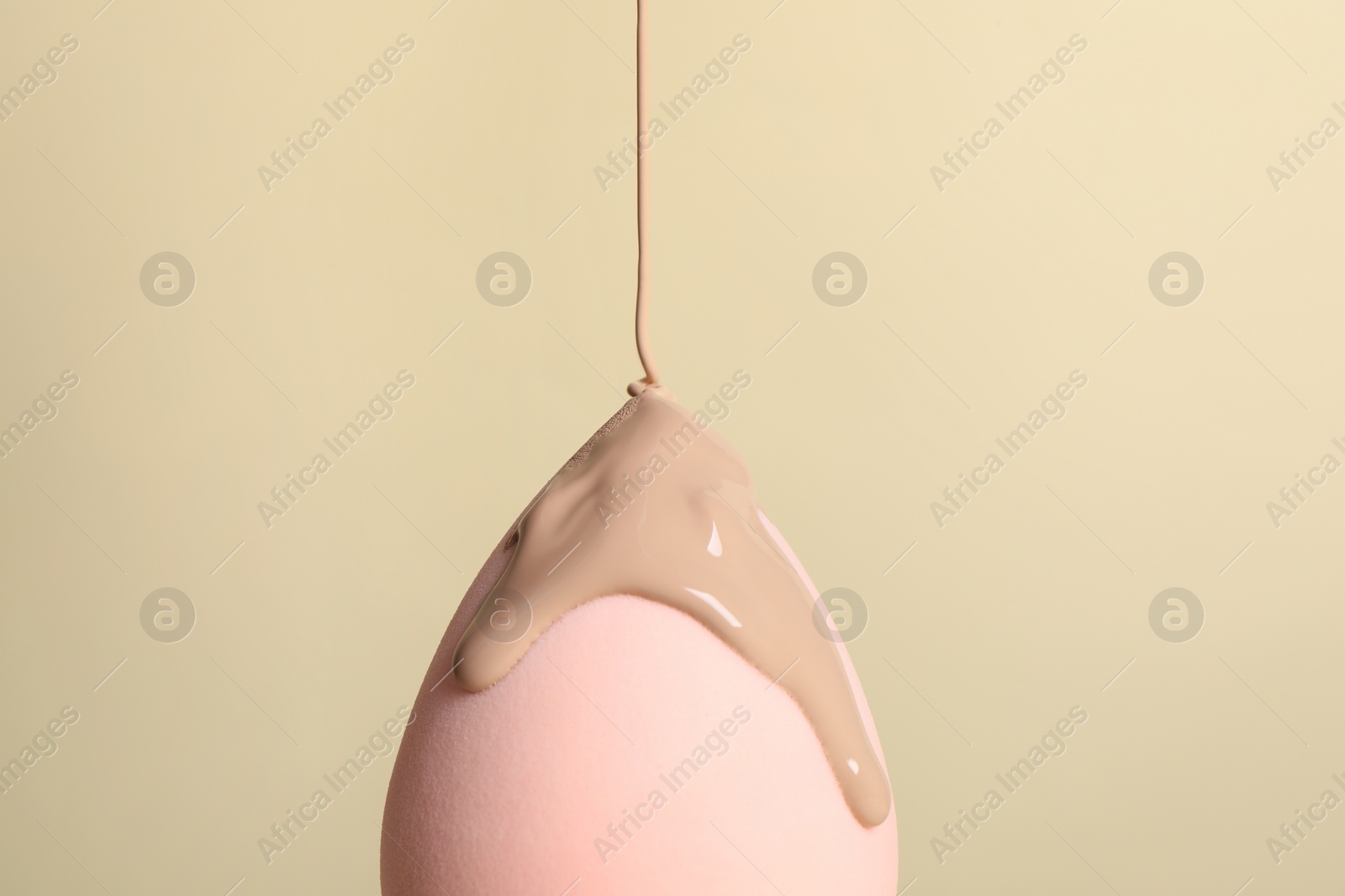 Photo of Skin foundation pouring onto makeup sponge on beige background