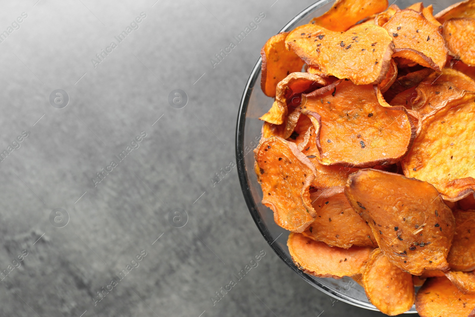 Photo of Bowl with sweet potato chips on grey table, top view. Space for text