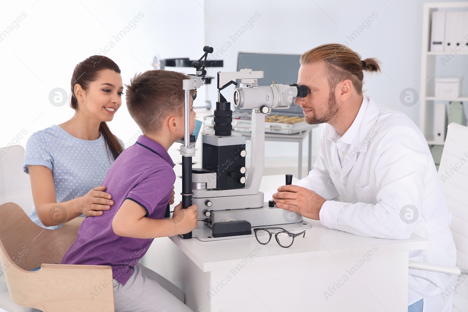 Photo of Children's doctor examining little boy with slit lamp in clinic