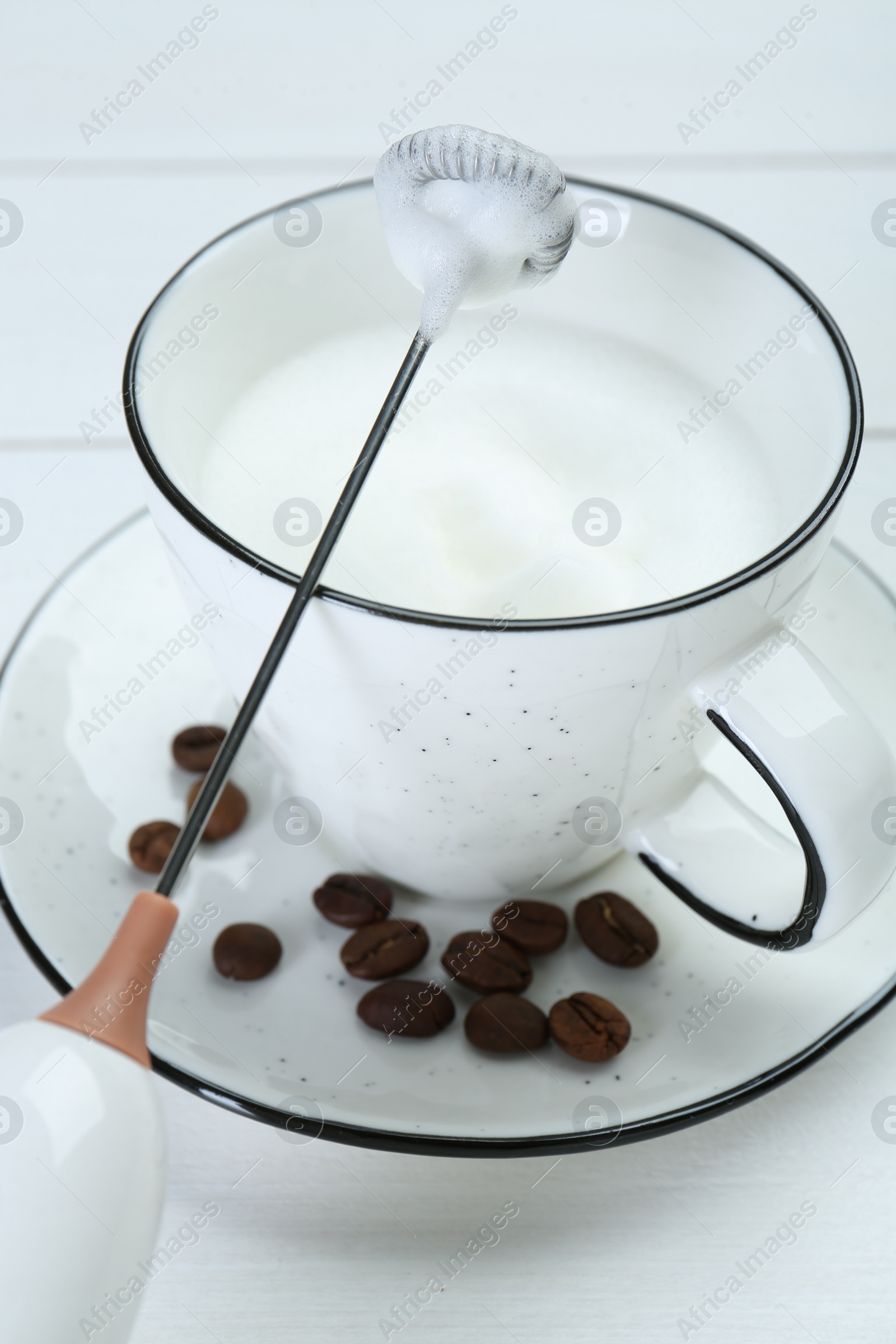 Photo of Mini mixer (milk frother), whipped milk and coffee beans on white wooden table, closeup