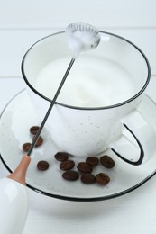 Photo of Mini mixer (milk frother), whipped milk and coffee beans on white wooden table, closeup