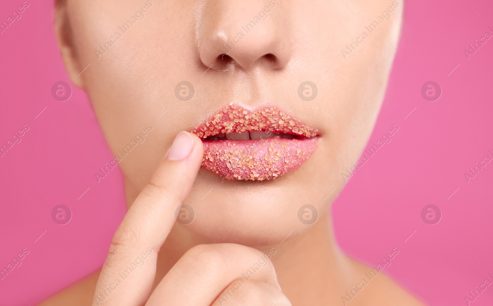 Photo of Young woman with sugar scrub on lips against pink background, closeup