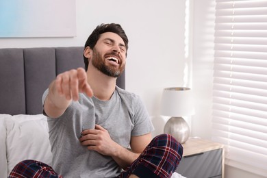 Photo of Handsome man pointing at something and laughing in bedroom. Space for text