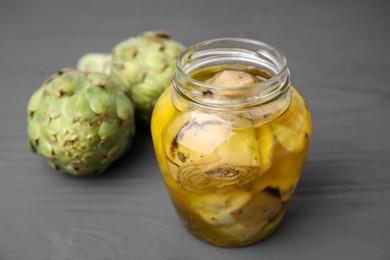 Pickled and fresh artichokes on grey wooden table, closeup