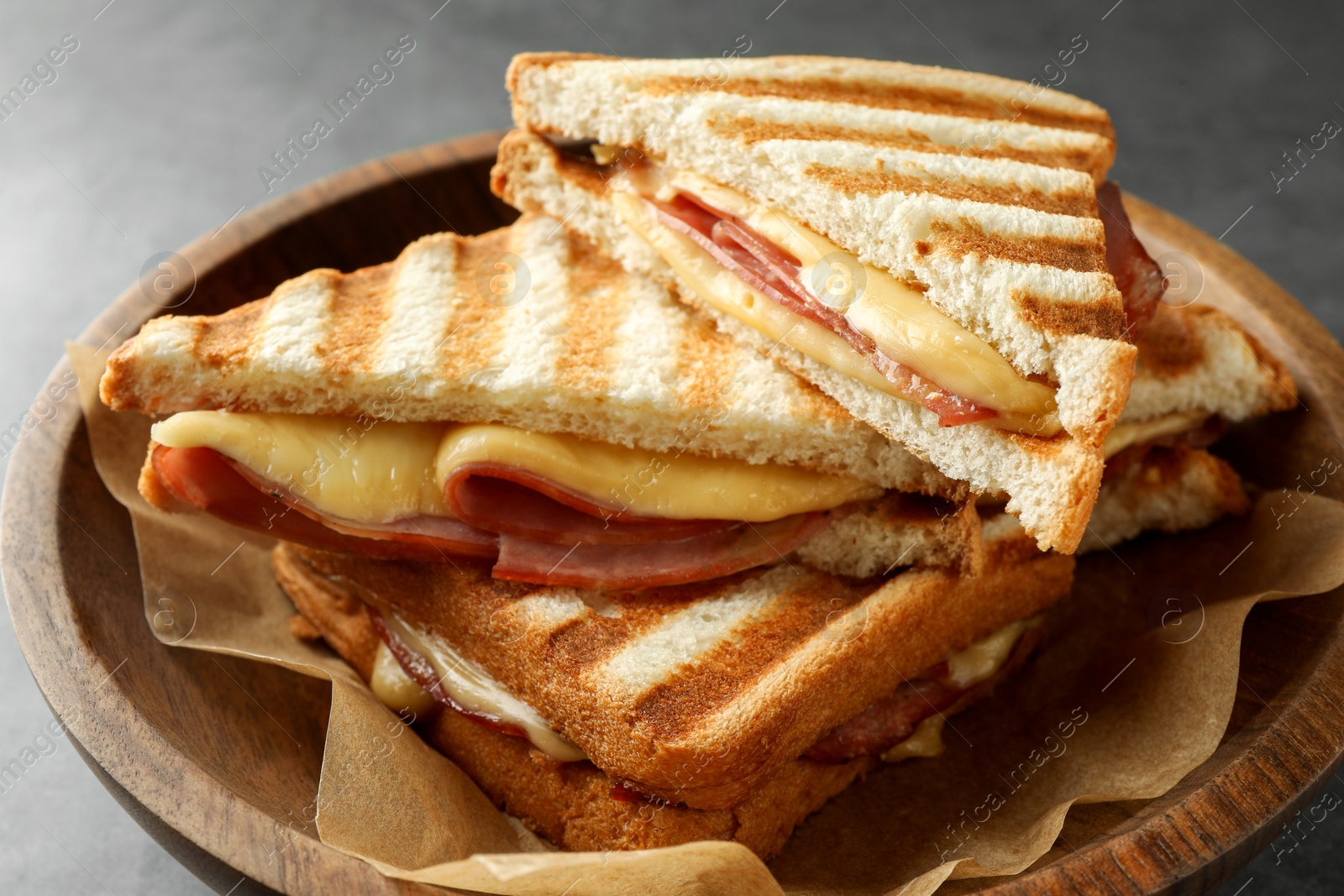 Photo of Tasty sandwiches with ham and melted cheese in bowl on table, closeup