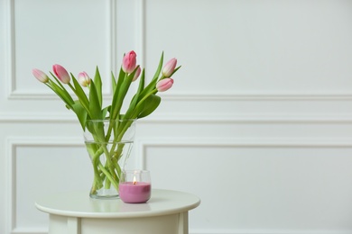 Beautiful tulips and burning candle on white table indoors, space for text. Interior design