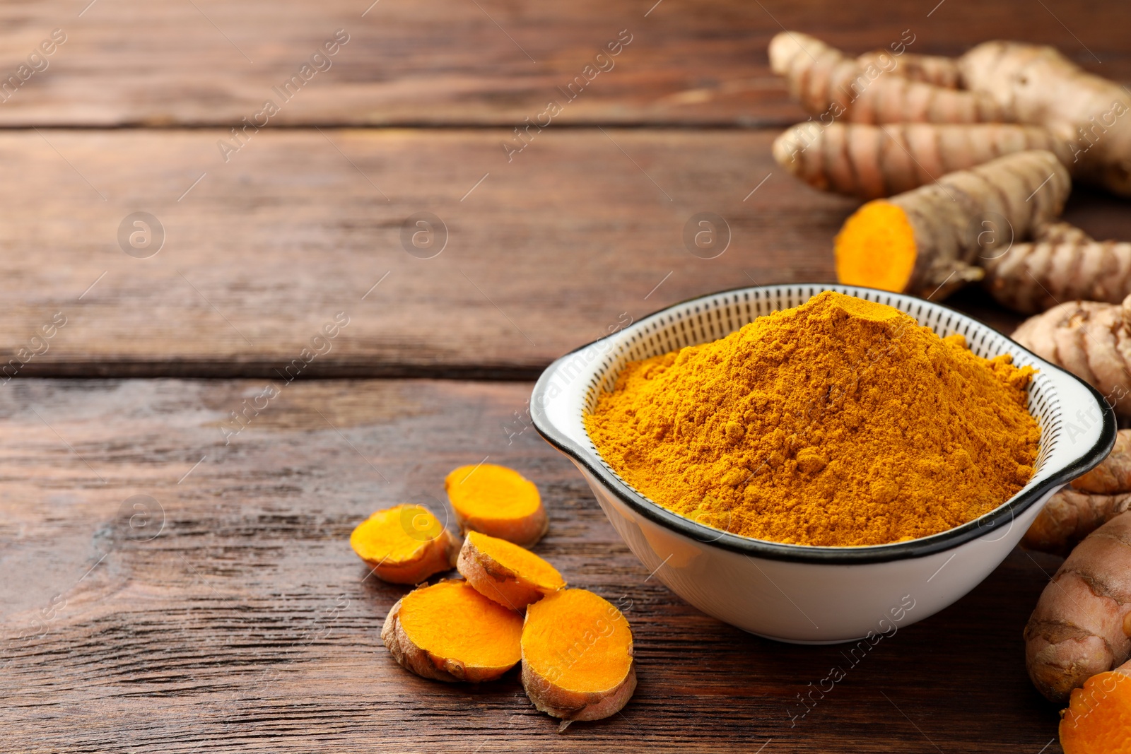 Photo of Bowl with aromatic turmeric powder and cut roots on wooden table. Space for text