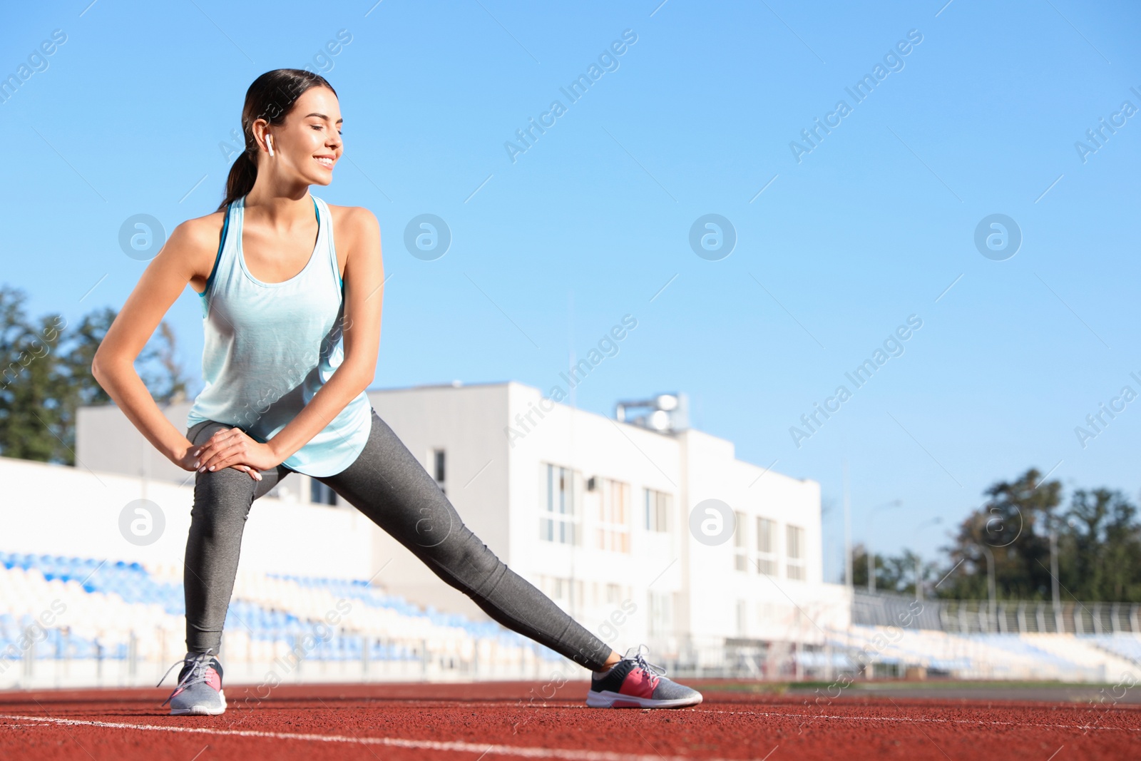 Photo of Young sportswoman with wireless earphones stretching at stadium