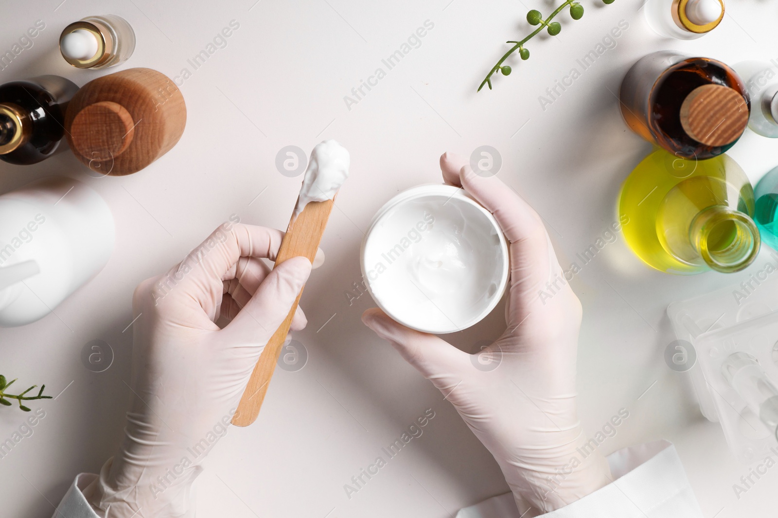 Photo of Dermatologist with jar testing cosmetic product at white table, top view