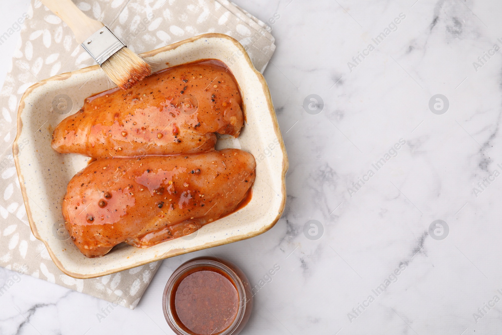 Photo of Raw marinated chicken fillets and basting brush on white marble table, flat lay. Space for text