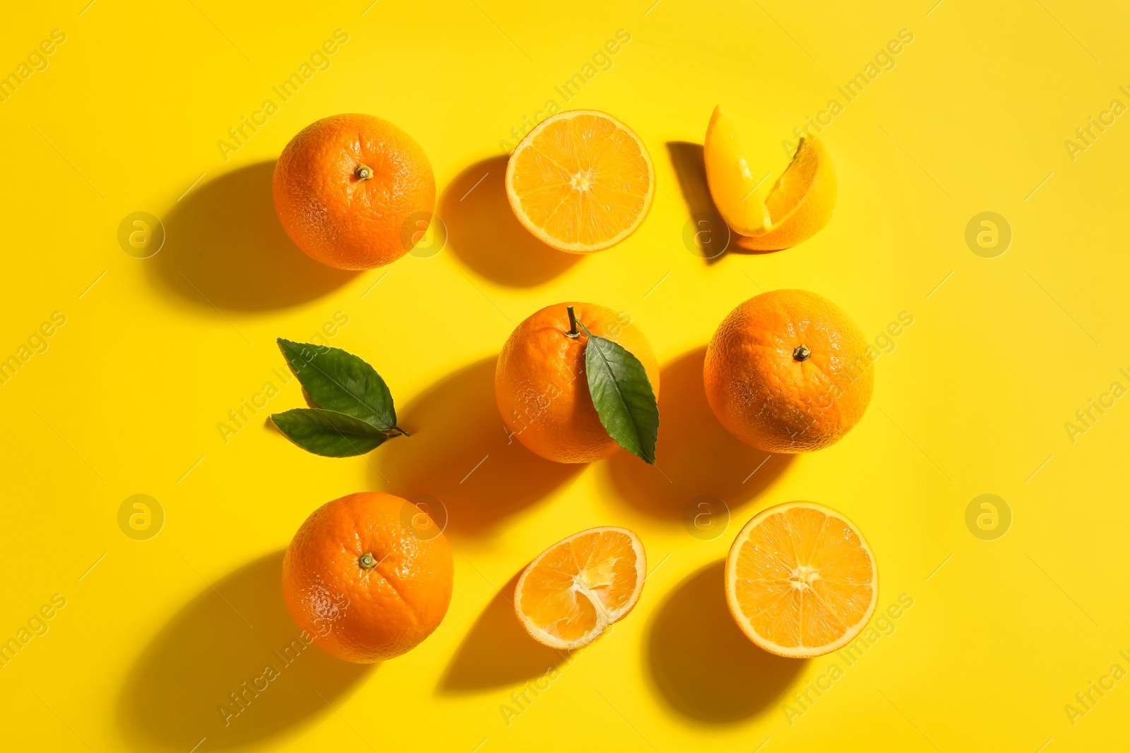 Photo of Fresh ripe oranges with green leaves on yellow background, flat lay