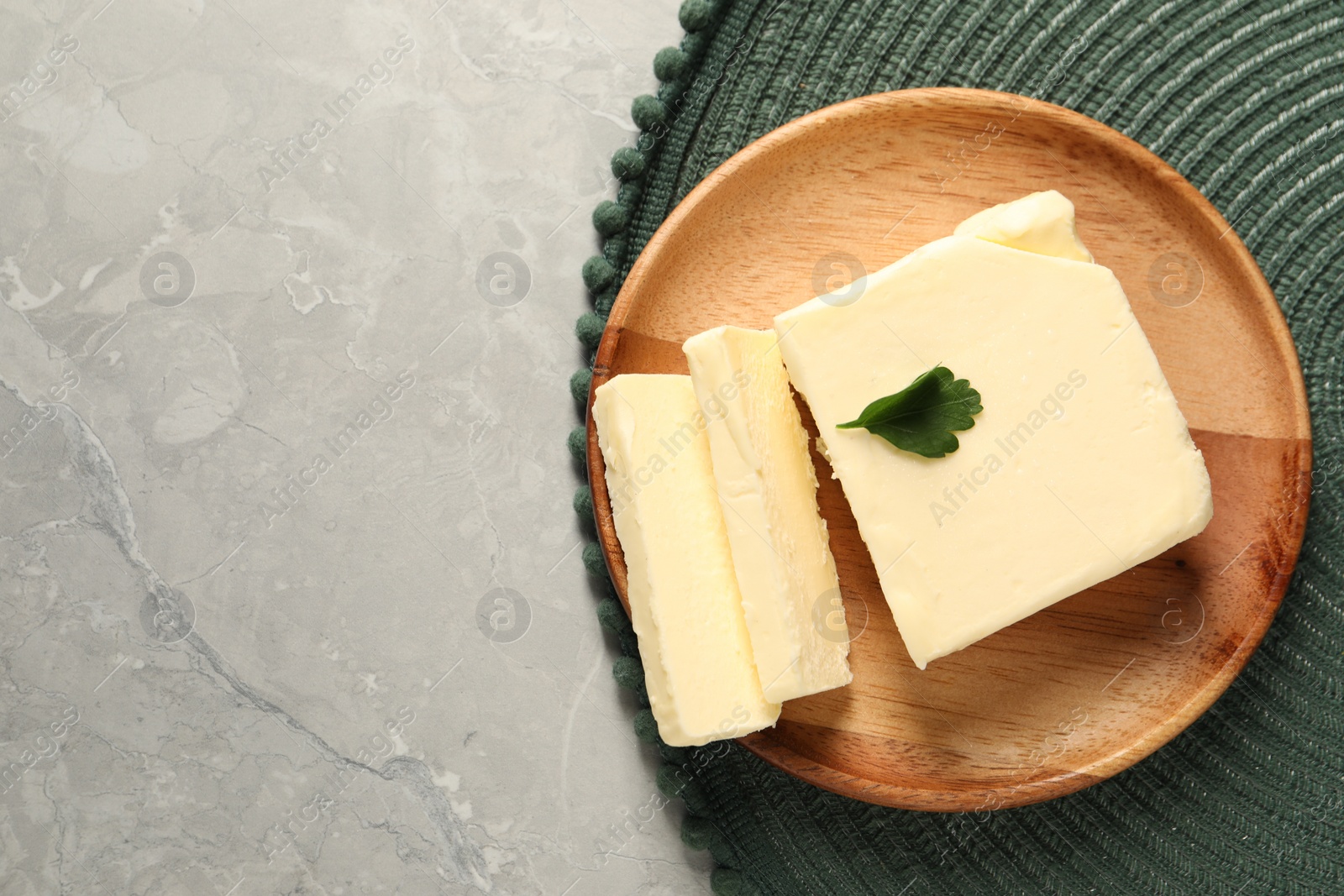 Photo of Cut tasty butter with parsley on grey table, top view. Space for text