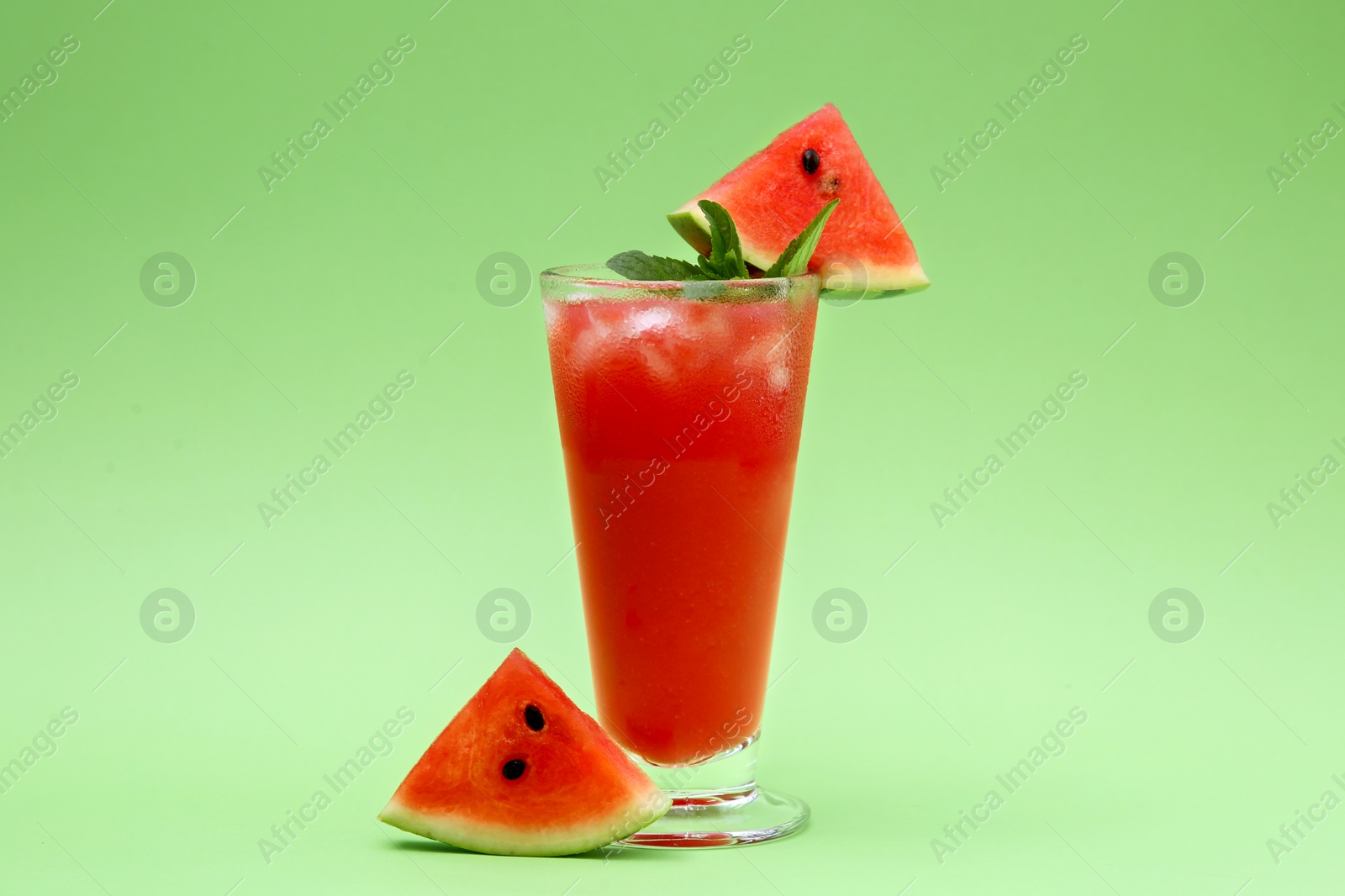 Photo of Glass of delicious drink with mint, ice cubes and cut fresh watermelon on light green background