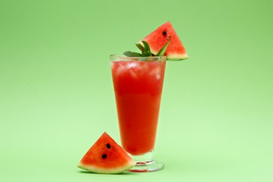 Glass of delicious drink with mint, ice cubes and cut fresh watermelon on light green background