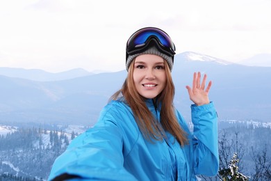 Smiling woman with ski goggles taking selfie in snowy mountains