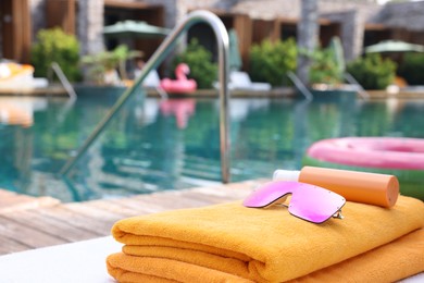 Beach towels, sunglasses and sunscreen on sun lounger near outdoor swimming pool at luxury resort closeup. Space for text