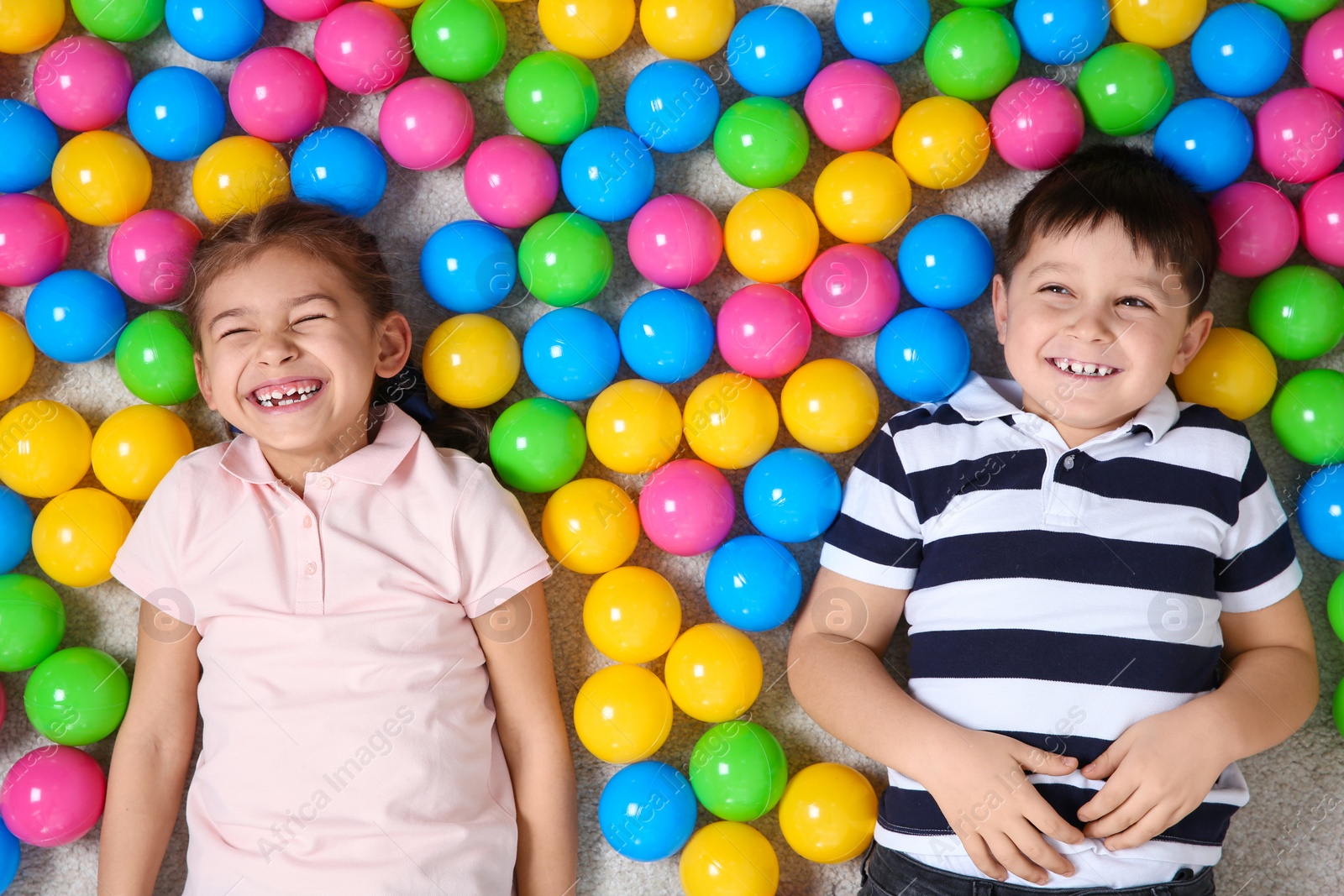 Photo of Cute children lying on floor near colorful balls, top view. Playing indoors