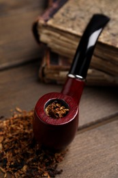 Photo of Smoking pipe and dry tobacco on wooden table, closeup