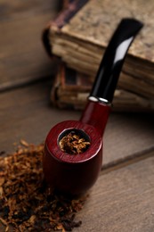 Smoking pipe and dry tobacco on wooden table, closeup