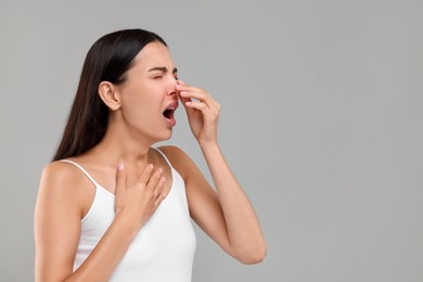 Photo of Suffering from allergy. Young woman sneezing on light grey background, space for text
