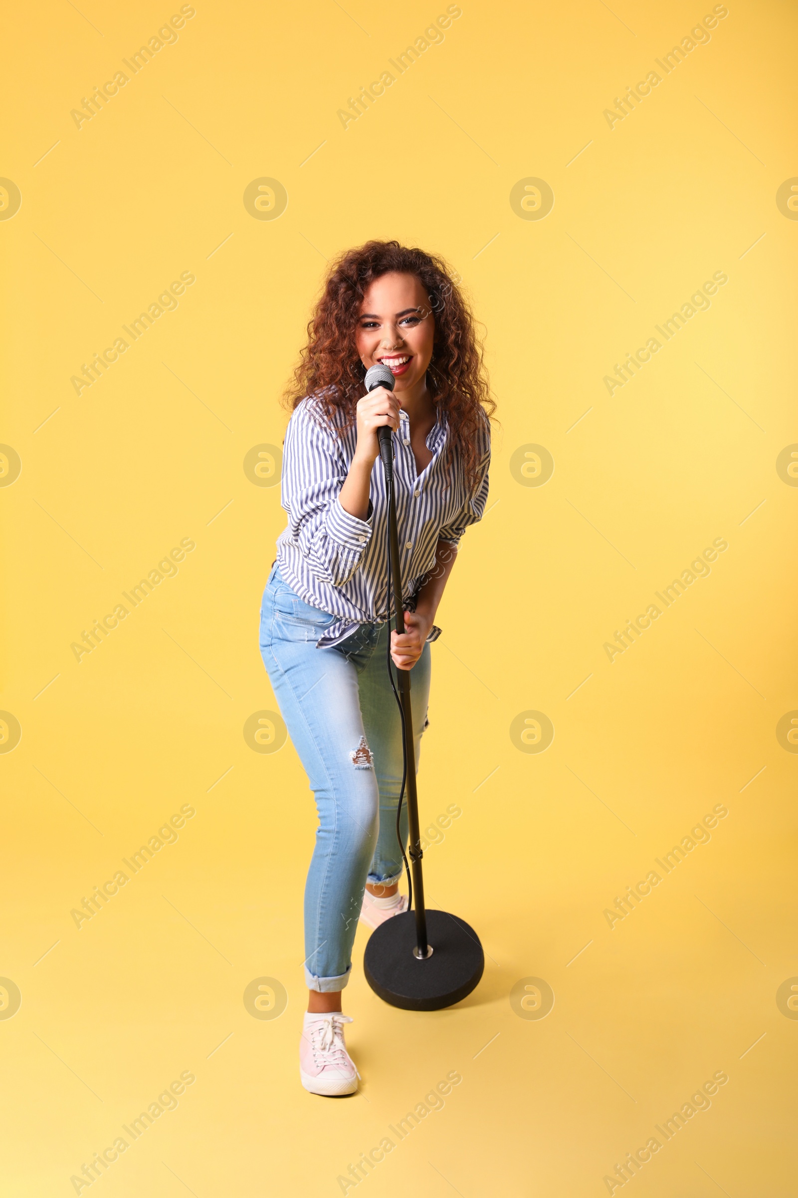 Photo of Curly African-American woman singing in microphone on color background