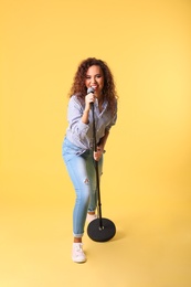 Photo of Curly African-American woman singing in microphone on color background