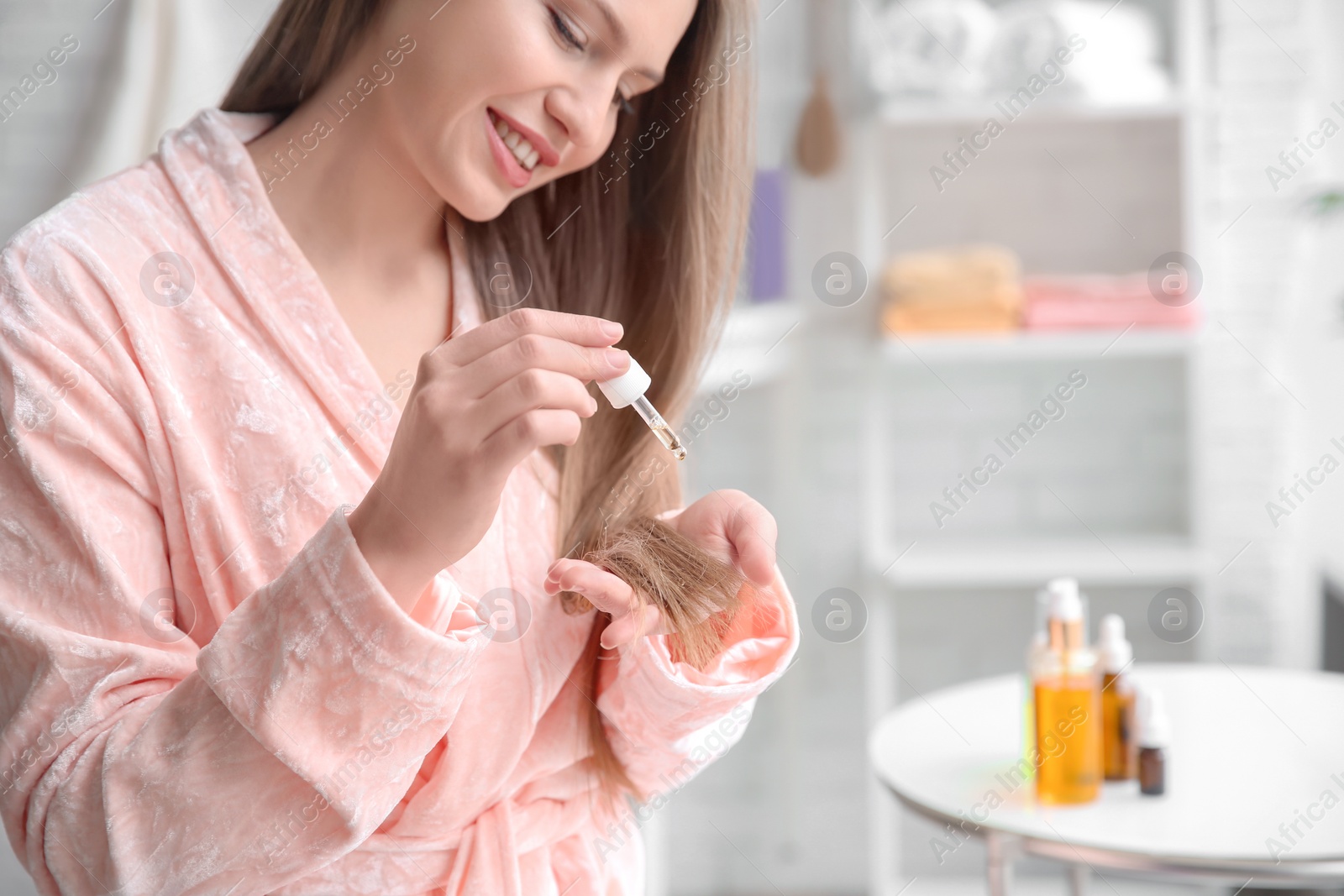 Photo of Young woman applying oil onto hair in bathroom