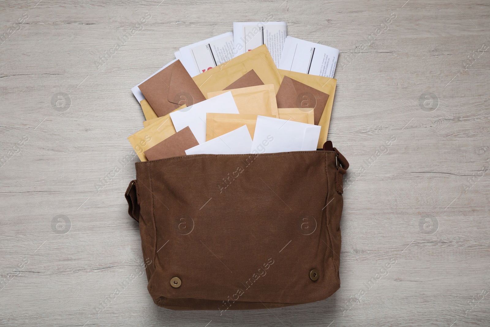 Photo of Brown postman bag with newspapers and mails on white wooden table, flat lay