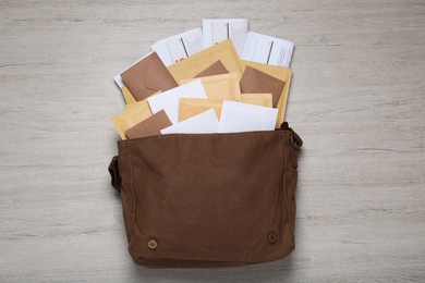 Photo of Brown postman bag with newspapers and mails on white wooden table, flat lay