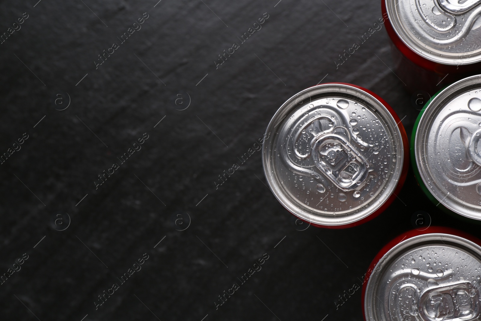 Photo of Energy drink in wet cans on black textured background, top view. Space for text