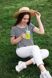 Photo of Young woman in straw hat with mason jar of fresh juice on green grass