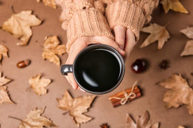 Photo of Woman in autumn sweater holding cup of hot cozy drink over color background, top view