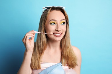 Fashionable young woman with bright makeup chewing bubblegum on light blue background