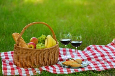 Photo of Wicker basket with food and wine on blanket in park, space for text. Summer picnic