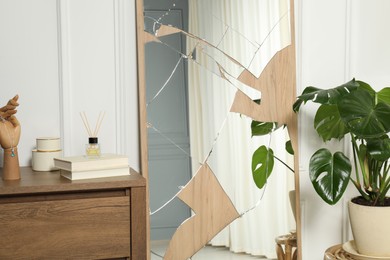 Photo of Broken mirror, houseplant, reed diffuser and books on wooden chest of drawers in room