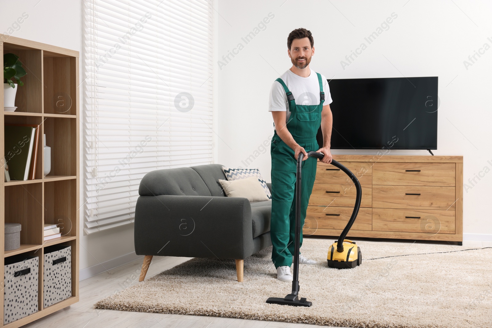 Photo of Dry cleaner's employee hoovering carpet with vacuum cleaner in room