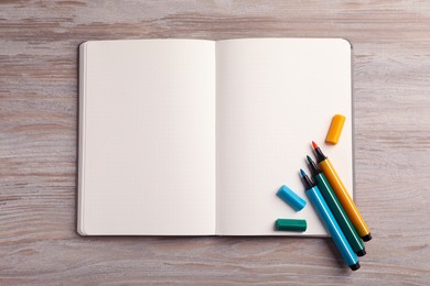 Open notebook and colorful markers on light wooden table, top view