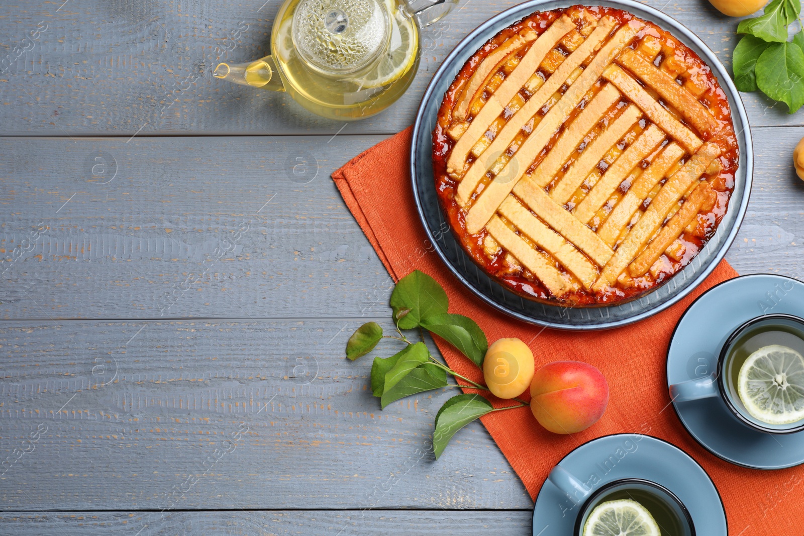 Photo of Tasty apricot pie and tea on grey wooden table, flat lay. Space for text