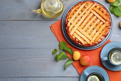 Photo of Tasty apricot pie and tea on grey wooden table, flat lay. Space for text