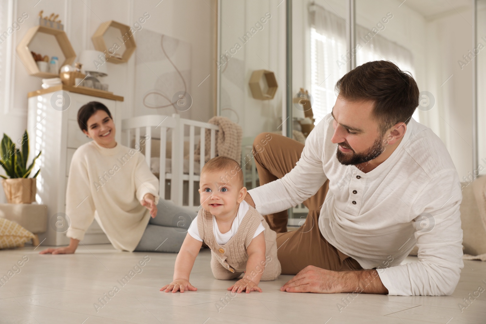 Photo of Happy parents helping their baby to crawl on floor at home