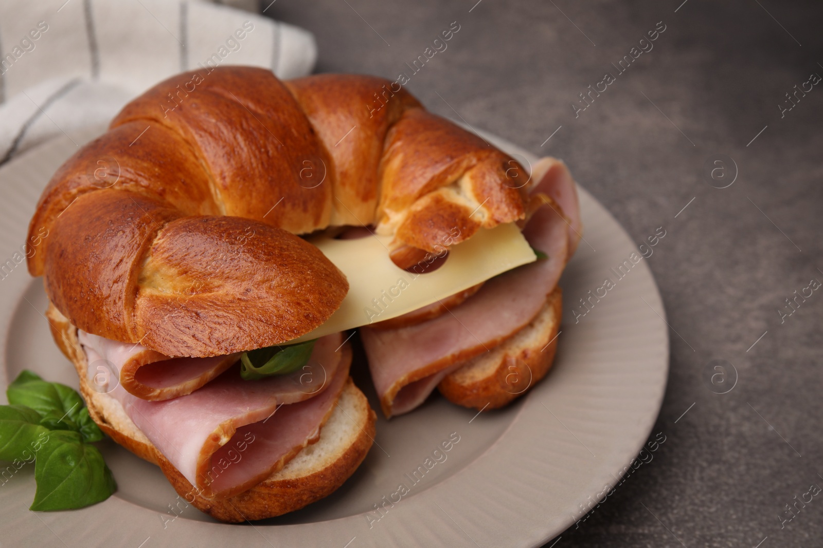 Photo of Tasty crescent roll with ham, cheese and basil on grey table, closeup